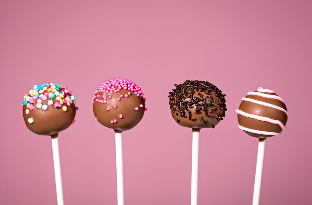 Chocolate cake pops with toppings against a pink background.